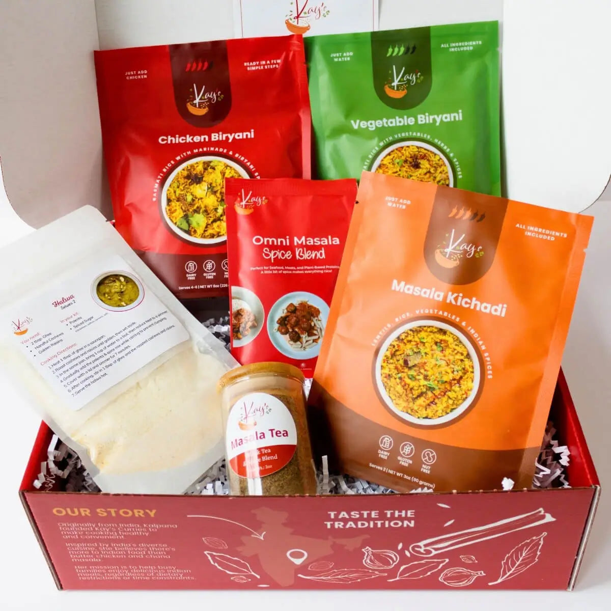 A gift box filled with Kay's Curries Kay's Curries Biryani Lover Gift Box, including red and green Chicken and Vegetable Biryani pouches, an orange Masala Kichadi pouch, a red Omni Masala Spice Blend pouch, a masala tea jar, and a white packaged item halwa, arranged in a red branded box.