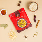 Red package of 'Chicken Biryani' with rice, spices, and a bowl of biryani on a beige background